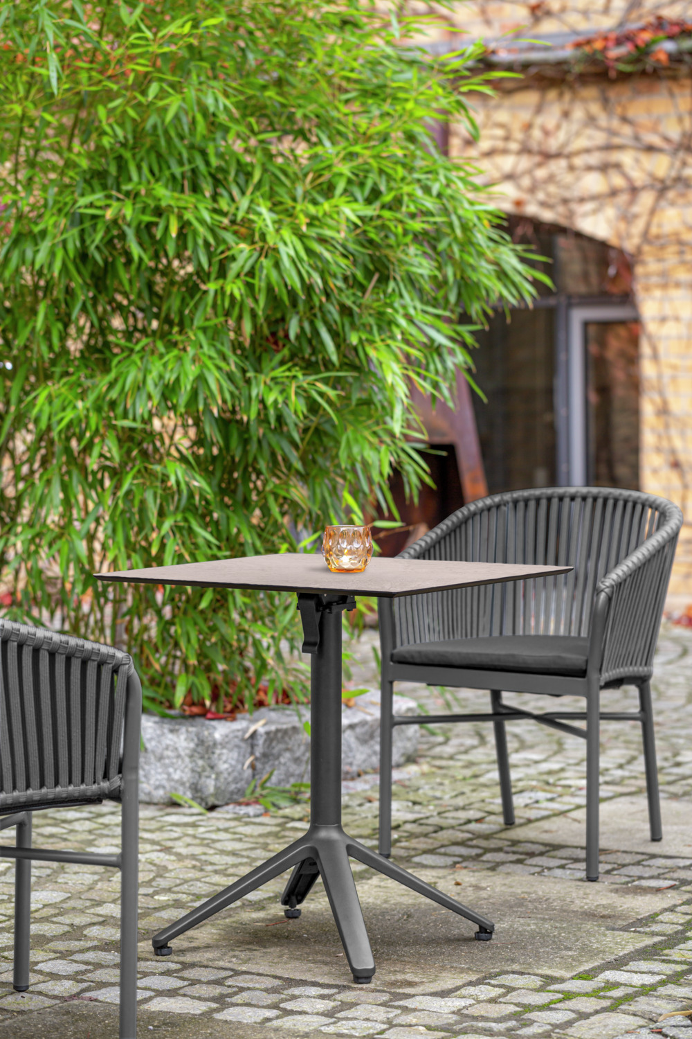 VEGA LUSINI Solutions GmbH Outdoor table Pachino Outdoor Bistrotisch Pachino Outdoor table Pachino; 80x80x73 cm (LxWxH); Table top concrete, base anthracite; square Outdoor Bistrotisch Pachino; 80x80x73 cm (LxBxH); Platte beton, Gestell anthrazit; quadratisch The outdoor table consists of a sturdy table base made of powder-coated aluminum and a scratch-resistant and robust table top Lift in the color concrete. The table base with foldable table cross and upright feet offer your guests more legroom. Table top thickness 1.3 cm. Suitable for outdoor use, UV-resistant and weatherproof. Delivery includes plastic adjustable glides. For assembly you need the mounting kit included with the table tops. Der Outdoortisch besteht aus einer stabilen Tischsäule aus pulverbeschichtetem Aluminium und einer kratzunempfindlichen und robusten Tischplatte LIFT in der Farbe beton. Die Tischsäule mit klappbarem Tischkreuz und hochstehende Füßen bieten Ihren Gästen mehr Beinfreiheit. Tischplattenstärke 1,3 cm. Für den Außenbereich geeignet, UV-beständig und wetterfest. Lieferung inklusive Verstellgleiter aus Kunststoff. Für die Montage benötigen Sie das den Tischplatten beiliegende Befestigungsset.